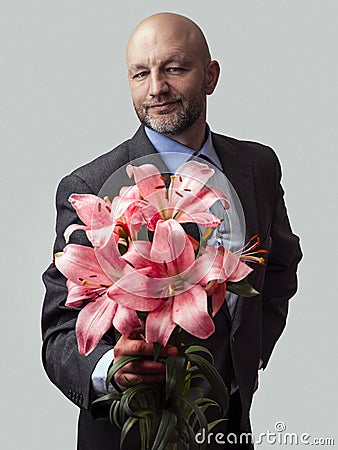 Man holding pink lily bouquet in his hands. Model is bald with grey beard, wearing classic grey suit. Handsome male with special Stock Photo