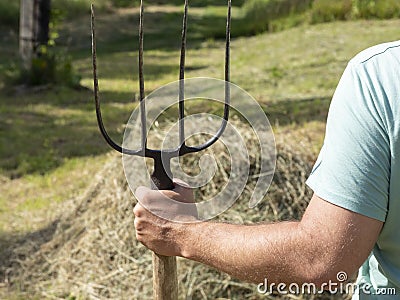 A man is holding a pitchfork. In the background is a haystack. Sunny day, summer. Concept of agriculture Stock Photo