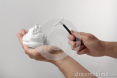 Man holding shaving foam and razor on light grey background, closeup Stock Photo