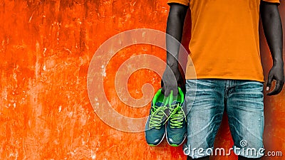 Man holding sport shoes in his hand on orange wall Stock Photo