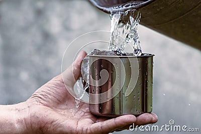 Man is holding a steel mug and a well water is pouring from a bucket Stock Photo