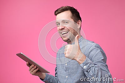 Man holding tablet raising thumbs up and smiling broadly, giving positive feedback Stock Photo