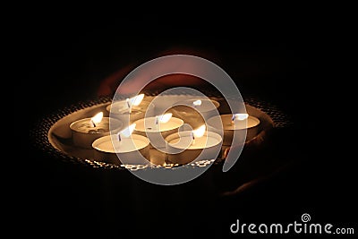 Man holding tealight wax candles or diya lamp in hand in dark night. Stock Photo