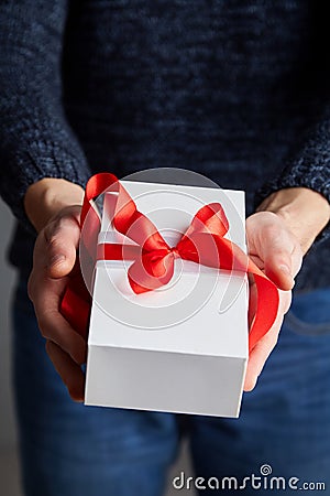 A man holding white gift box with red ribbon in his hands Stock Photo