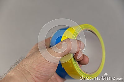 A man is holding yellow and blue duct tape in his hand. Reel of colored duct tape against the gray background. Selective focus. No Stock Photo