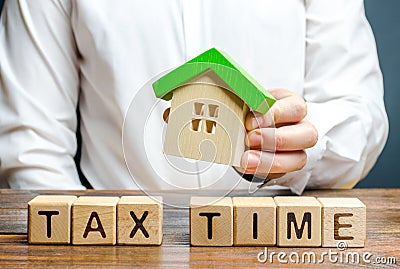 A man holds a figure of a house above the inscription Tax Time. Taxation, income tax. Declaring income, countering the shadow Stock Photo