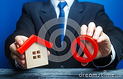 A man holds a house and the red prohibition symbol NO. Bank refuses to provide a mortgage loan. Housing problems. Confiscation Stock Photo