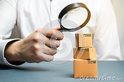 A man holds a magnifying glass above the boxes. Examination of goods for the presence of contraband, prohibited goods, defects. Stock Photo