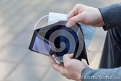 Man holds a medical mask and empty wallet without money. Bankruptcy and unemployment resulting from the global coronavirus Stock Photo