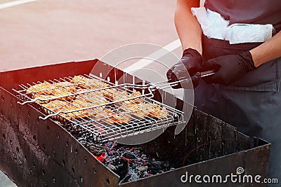 A man holds a mesh for a barbecue. Burning coals in the grill. He is wearing black medical gloves and an apron.Picnic in the city Stock Photo