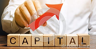 Man holds red arrow up above word Capital. Increase investment and foreign capital in the national economy. Improve business Stock Photo