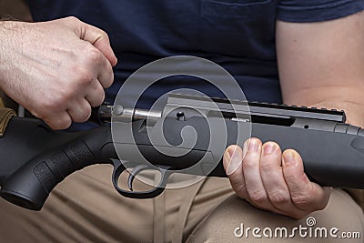 A man holds a rifle on his knees, pulls back the bolt, reloads the weapon. Concept: storage and use of firearms. Stock Photo