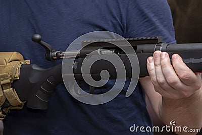 A man holds a rifle on his knees, pulls back the bolt, reloads the weapon. Concept: storage and use of firearms. Stock Photo