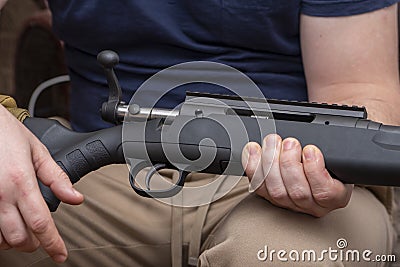 A man holds a rifle on his knees, pulls back the bolt, reloads the weapon. Concept: storage and use of firearms. Stock Photo