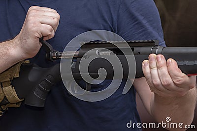 A man holds a rifle on his knees, pulls back the bolt, reloads the weapon. Concept: storage and use of firearms. Stock Photo