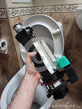 A man holds a toilet flush mechanism after repair, plumbing repair, white toilet bowl in the interior top view, toilet interior Stock Photo