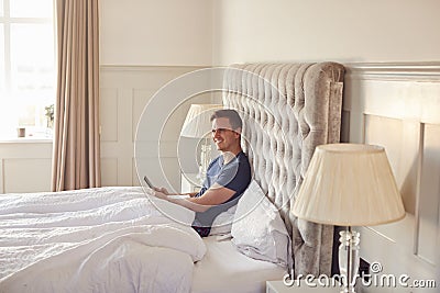 Man At Home In Bed Self Isolating Using Digital Tablet And Mobile Phone During Covid 19 Lockdown Stock Photo