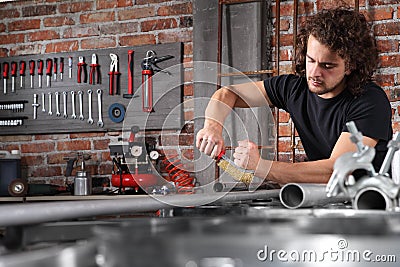 Man in home workshop garage work metal with handle wire brush, repair, brushes and cleaning iron pipe on the workbench full of Stock Photo