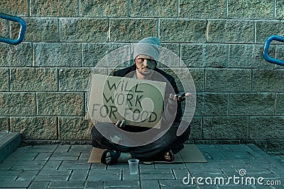 A man, homeless, a man asks for alms on the street with a sign will work for food. Concept of homeless person, addict, poverty, Stock Photo