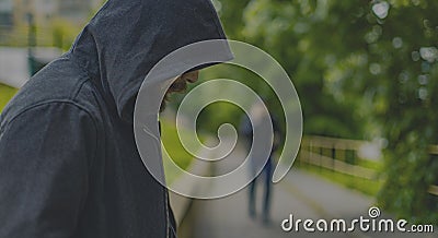 Man in hoodie looking like criminal person stay alone on park outdoor street walk way site and wait for a victim, human silhouette Stock Photo