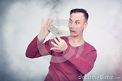 Man in horror looks at a smartphone burning in his hands. Mobile device fire situation Stock Photo