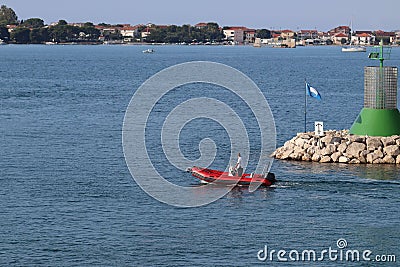 A man in an inflatable motorboat, swims past a stone breakwater with a dangerous signal beacon. Rest on the water in paradise. Editorial Stock Photo