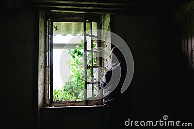 A man inside an old crumbling house near the window. Depression, loneliness, despair, decline, sadness concept Stock Photo