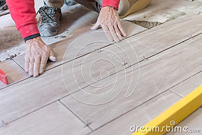 Man installing rectangular shaped floor tiles in kitchen. Applying adhesive before installation and verifying afterwards Stock Photo