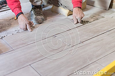 Man installing rectangular shaped floor tiles in kitchen. Applying adhesive before installation and verifying afterwards Stock Photo