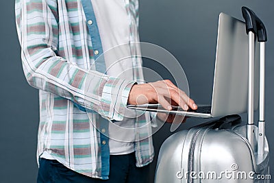 Man isolated on gray wall tourism concept standing with suitcase typing message on laptop close-up Stock Photo