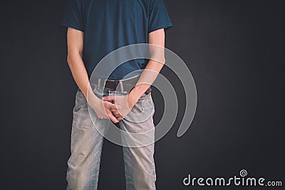 Man in jeans covers his crotch with hands against black wall Stock Photo