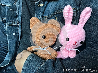 Man in jeans jacket holding cute brown teddy bear and pink bunny crochet dolls Stock Photo