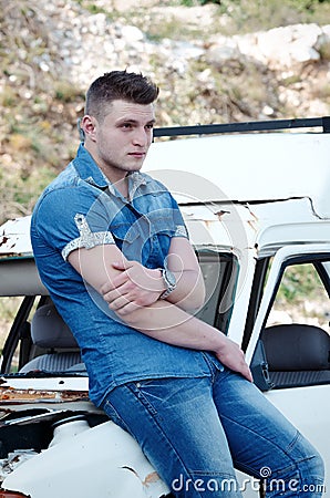 Man in jeans, sitting on an old damaged car Stock Photo