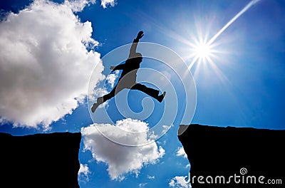 Man jumping across the gap from one rock to cling to the other. Stock Photo