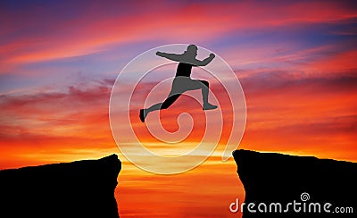 Man jumping across the gap from one rock to cling to the other. Stock Photo
