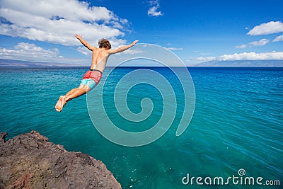 Man jumping off cliff into the ocean Stock Photo