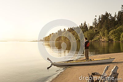 Man with kayak on beach looking out at water. Solo outdoor adventure sports sea kayaking in beautiful, remote nature wilderness Stock Photo