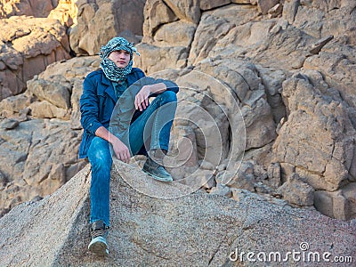 Man in a keffiyeh sitting on a rock in the desert Stock Photo