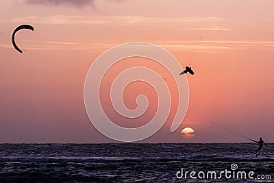Man kitesurfer athlete jumping at sunset, silhouette at dusk. Kite surfer man doing board off kiteboarding trick orange Editorial Stock Photo