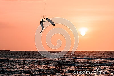 Man kitesurfer athlete jumping at sunset, silhouette at dusk. Kite surfer man doing board off kiteboarditrick on orange packgroung Editorial Stock Photo