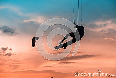 Man kitesurfer athlete jumping at sunset, silhouette at dusk man doing board grab. Kitesurfing sport on orange background Editorial Stock Photo