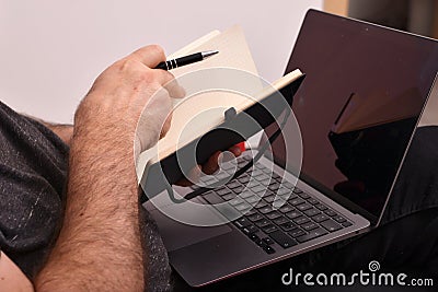 A man with a laptop on his lap taking notes in a notebook, close-up, online business analysis Editorial Stock Photo
