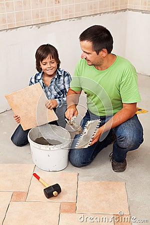 Man laying ceramic floor tiles helped by small boy Stock Photo