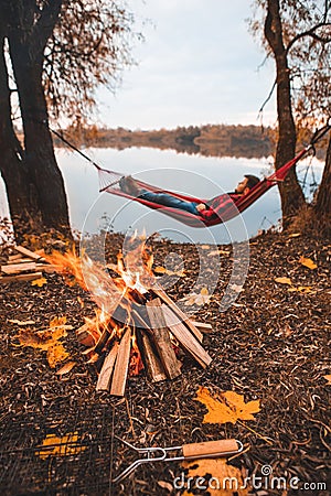 man laying dawn in hammock at autumn lake view. bonfire. camping concept Stock Photo