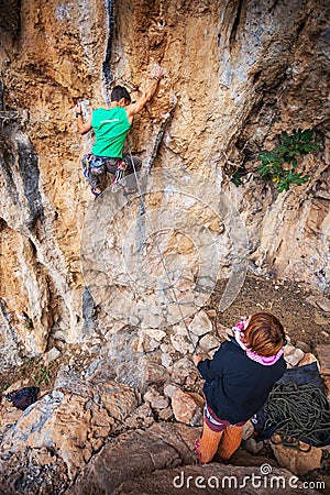 Man lead climbing on a cliff, belayer watching him Stock Photo