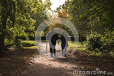 Man leaning on a wooden crutch walking hand in hand with woman in the Hexthorpe park. Editorial Stock Photo