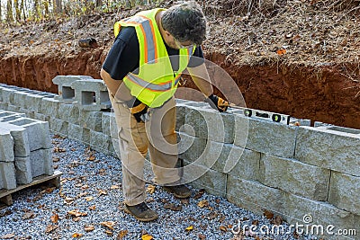 Man with leveling tool building retaining block wall with being built on new property Stock Photo