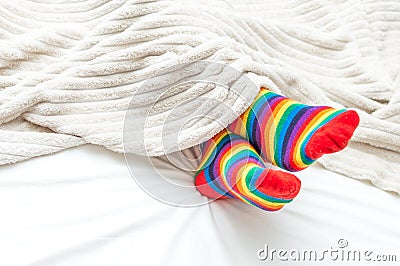 A man lies in a bed under a rug in socks of rainbow colors. LGBT concept. Close-up Stock Photo