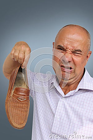 A man in a light shirt holds a brown male shoe in his hand, a grimace of disgust from the bad smell on his face, close-up, copy Stock Photo