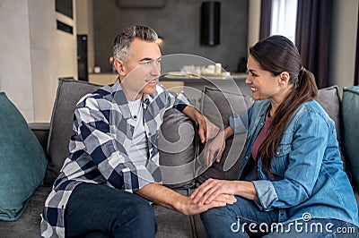 Man listening happy woman sitting on sofa Stock Photo